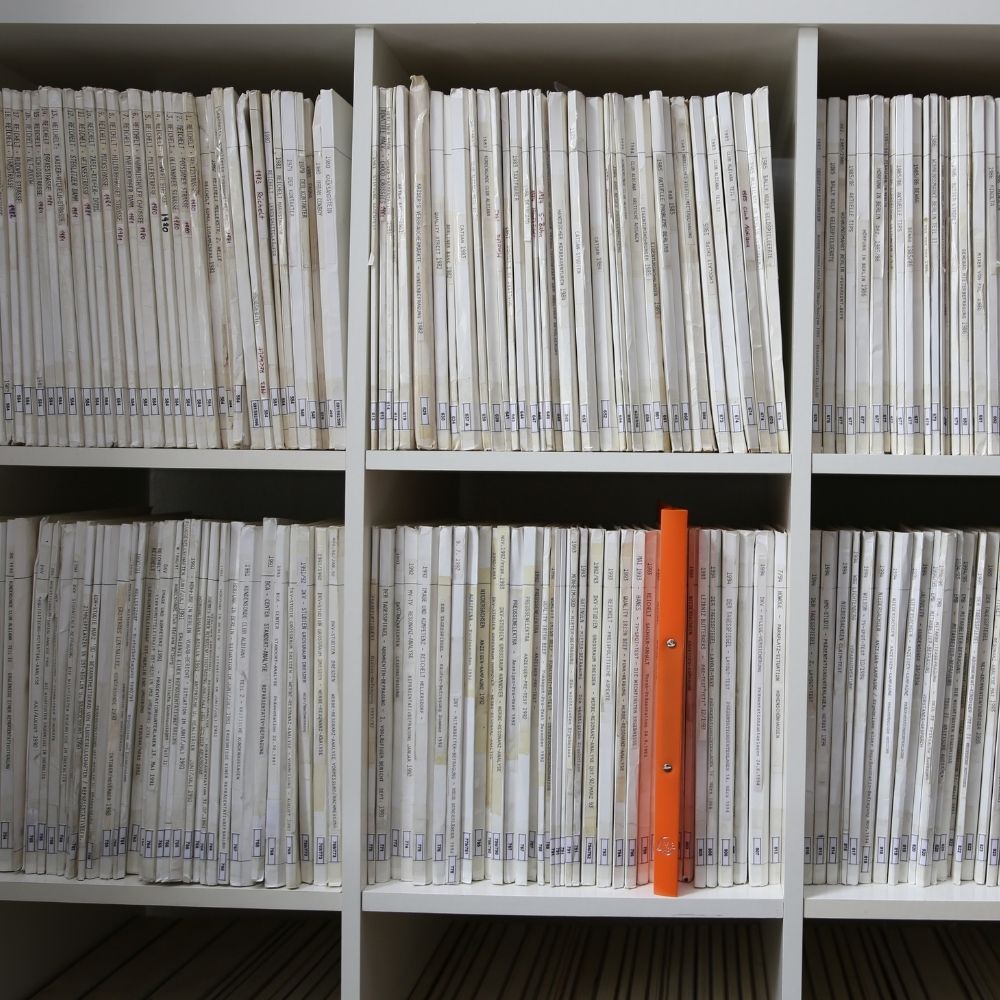 bild von einem regal mit vielen weißen büchern, darunter ein buch in orange, welches etwas raussteht